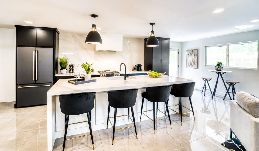 Modern kitchen with marble island, black cabinetry, bar stools, and natural light.