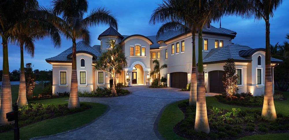 Elegant luxury home at dusk with palm trees and warm glowing lights.