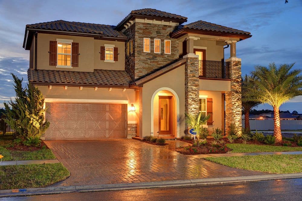 Modern two-story home with stone accents, illuminated driveway, and palm trees at dusk.