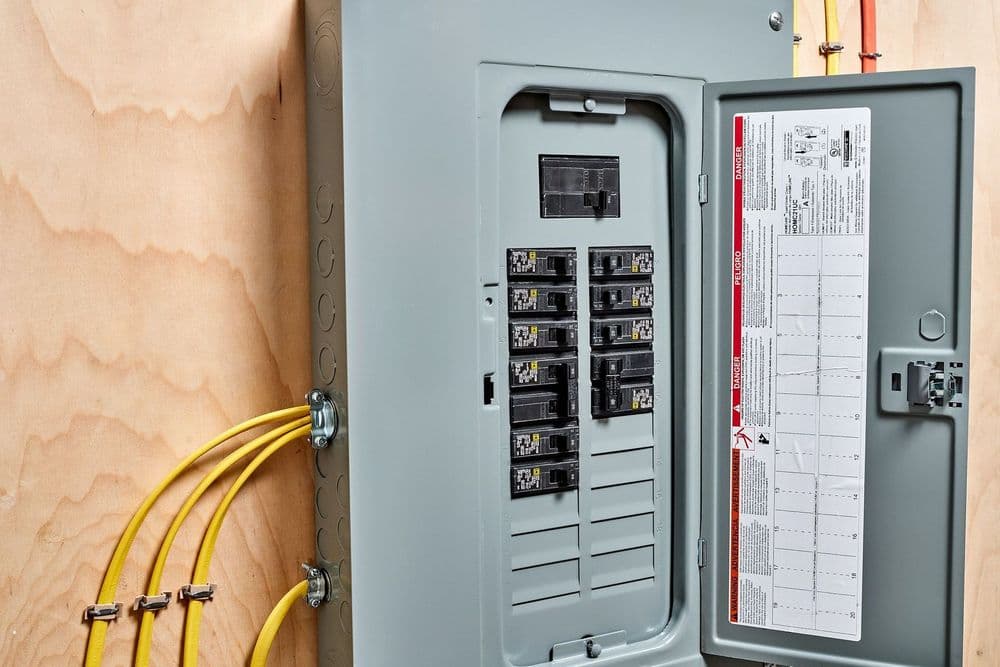 Electrical panel with circuit breakers and yellow wiring on a wooden wall.