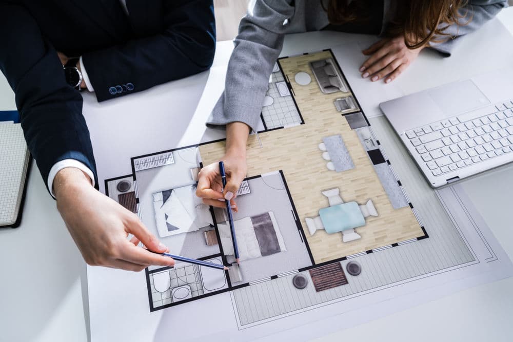 Two professionals discussing a floor plan design, reviewing layouts and details at a table.