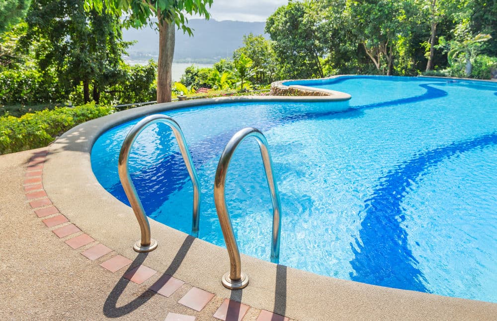 Serene swimming pool with clear blue water surrounded by lush greenery and scenic views.