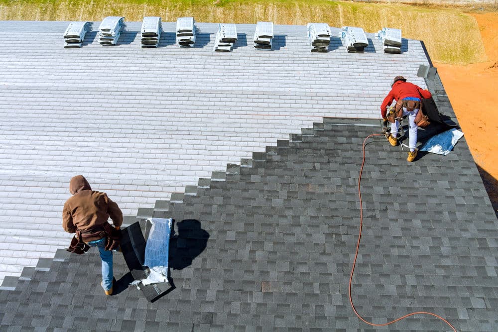 Roofers installing shingles on a new roof, with vents visible in the background.