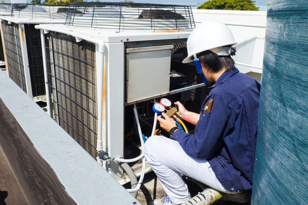 HVAC technician servicing outdoor unit with pressure gauges on rooftop.